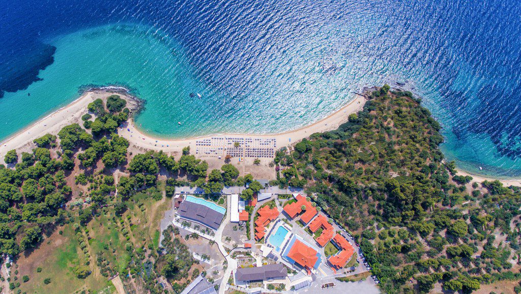 Aerial view of Lagomandra Beach with turquoise sea and pine forest from a bird’s-eye perspective