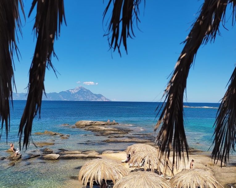 Palm leaves framing the rocky bay of Tigania Beach in Sithonia with Mount Athos in the background