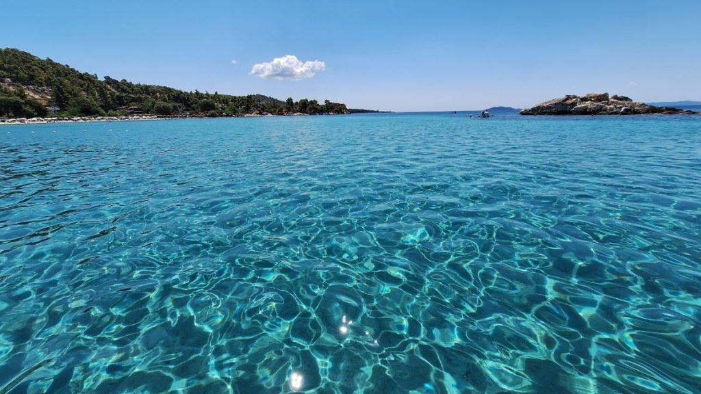 Crystal-clear turquoise water with a small island in the background at Kalogria Beach, Sithonia, Halkidiki