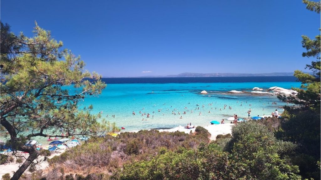 View of Orange Beach with white sand, turquoise water, and a few people swimming, Sithonia, Halkidiki