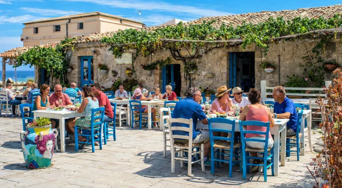 Traditional Greek taverna with people enjoying food at seaside tables with blue chairs and rustic stone buildings