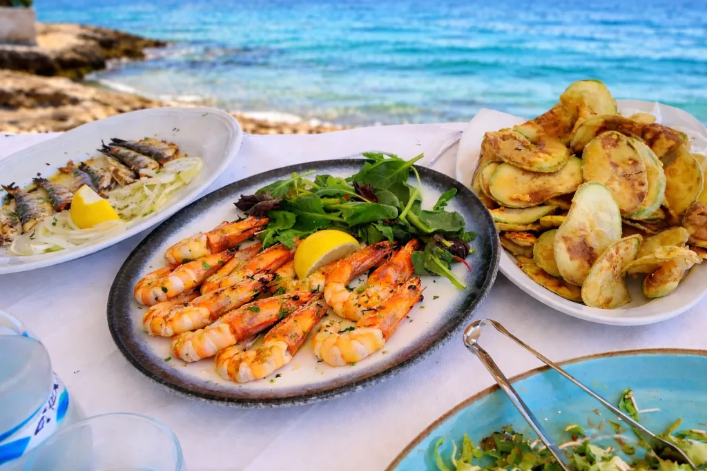 Grilled shrimp and zucchini served on a rustic table in a seaside taverna with a blurred ocean view in the background