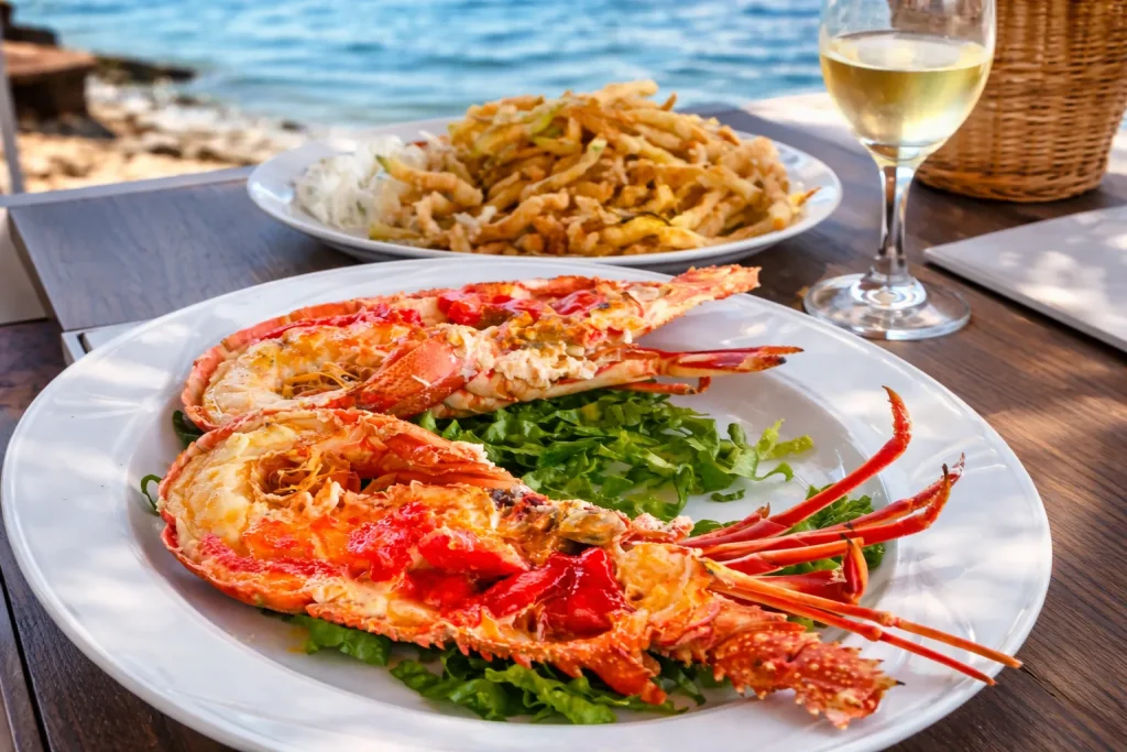 grilled lobster with fried zucchini and white wine on seaside restaurant table in Greece