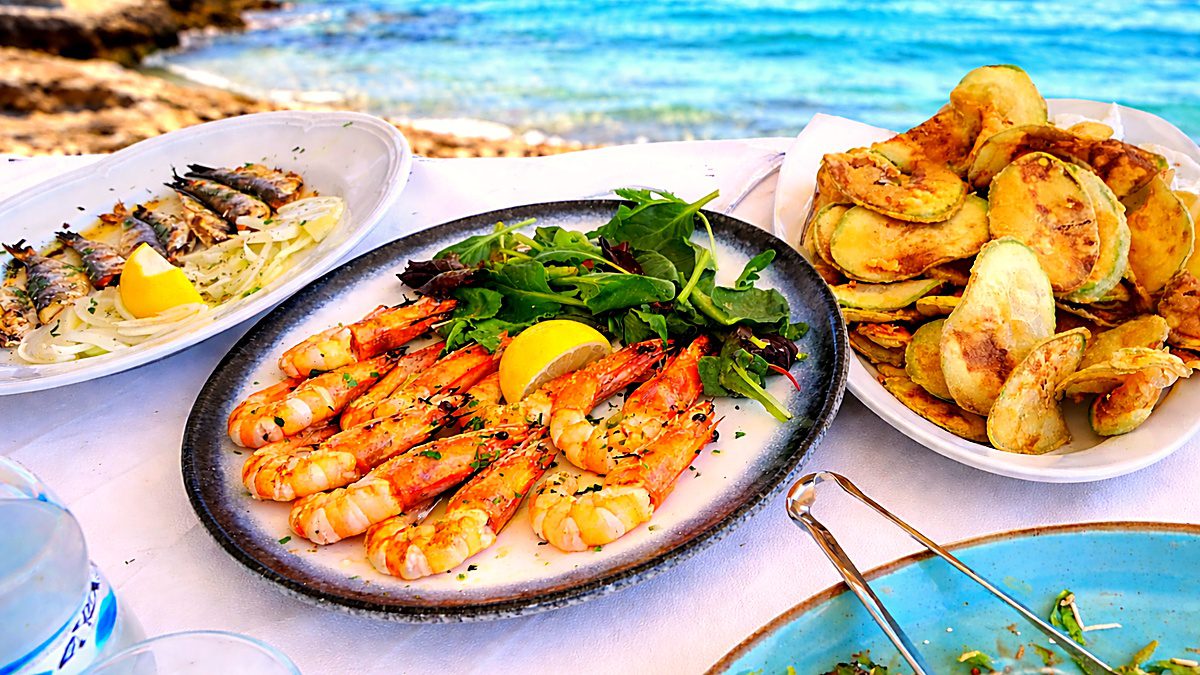 Grilled shrimp and zucchini served on a rustic table in a seaside taverna with a blurred ocean view in the background